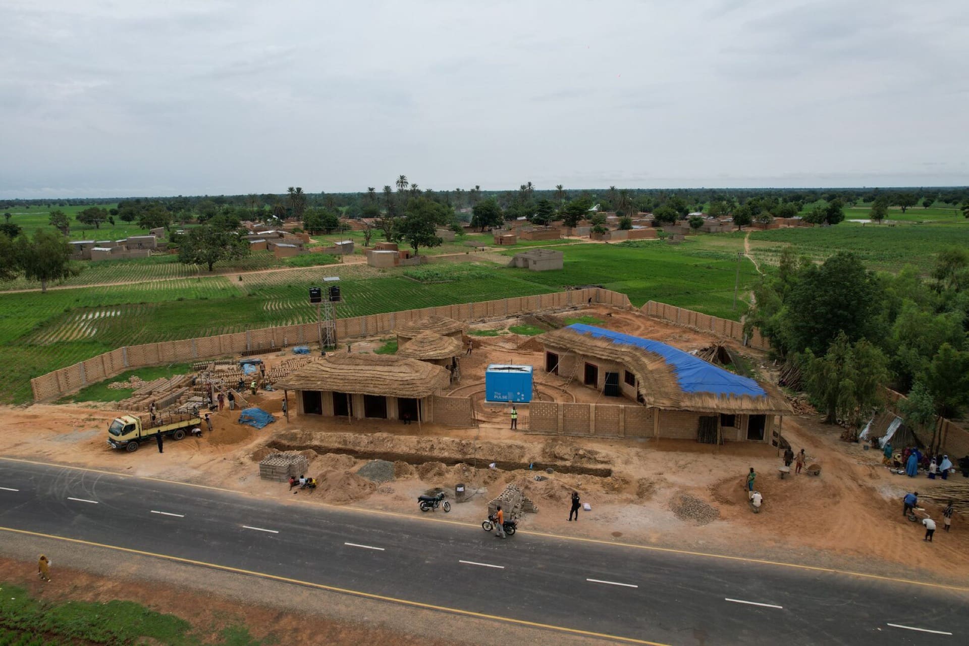 Build crew assembling a PULSE Centre — frame up, panels staged, community foreground.